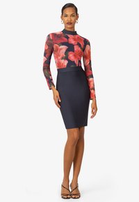 Abito aderente con maniche lunghe a stampa floreale in rosso e verde su sfondo blu navy, abbinato a una gonna a sigaretta di un blu navy scuro uniforme.