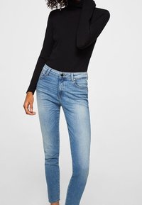 Suéter de cuello alto de manga larga negro combinado con vaqueros ajustados de color azul claro, que presentan un diseño clásico de cinco bolsillos y un sutil desgastado en las piernas.