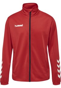 Rød sportjakke med høj krave og fuld lynlås. Har hvidt logo på venstre bryst og hvide chevronmønstre på ærmerne. Glat tekstur.