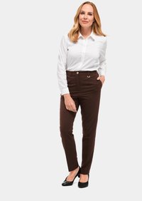 Bruine op maat gemaakte broek met een hoge taille, zakken en een voornaaikreuk. Gekoeld met een witte button-down blouse en zwarte pumps.