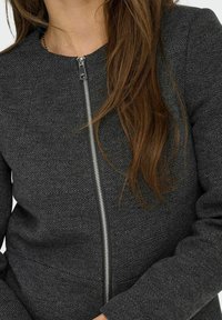 Veste zippée en chevron gris avec un col rond. Caractéristiques d'une fermeture éclair argentée et d'un tissu texturé. Design ajusté avec des manches longues.