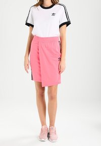 Bílé tričko s černými detaily a logem, doplněné růžovými šortkami s šňůrkou v pase a černými proužky po stranách. Růžové tenisky.