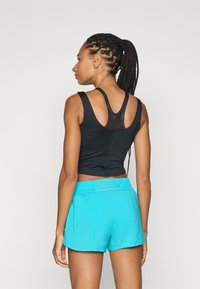 Crni sportski crop top s dizajnom racerback u kombinaciji s svijetloplavim šortsevima, koji imaju elastičnu trakicu u struku i glatku teksturu.