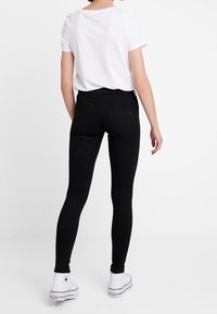 Vaqueros negros ajustados con una cintura de media altura, tela elástica y textura suave, combinados con una camiseta blanca lisa y zapatillas blancas.