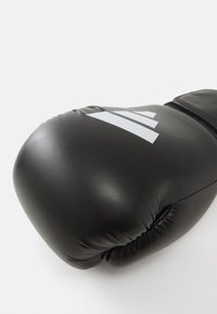 Svart boxhandske i läder. Har en slät yta med en rund form och grå Adidas-logotypdetaljer.
