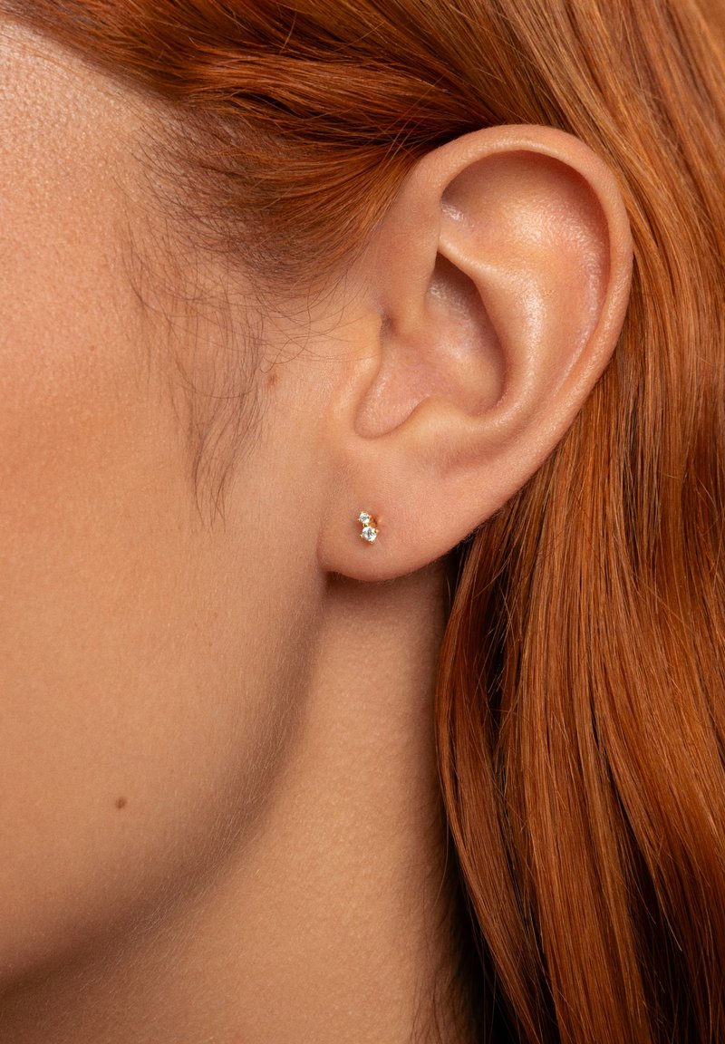 Boucles d'oreilles en or avec des pierres précieuses transparentes, présentant un design simple. Le sertissage est affleurant au lobe de l'oreille, mettant en valeur la clarté des gemmes.