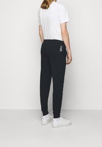 Jogging en marine avec une coupe ajustée, une taille élastique et des poches latérales. Doté d'un détail de bande décorative sur la poche arrière.