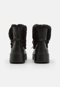 Sorte lær ankle boots med bløtt svart pelsfôr, rund tå og tykk plattformsåle. Har lisser og en løkke bak.