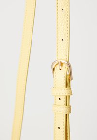 Cinghia per borsa in finta pelle gialla con superficie texturizzata, fibbia regolabile e più fori per le regolazioni della lunghezza. Accenti in metallo color oro.
