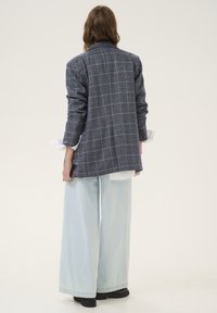 Marineblauer karierteter Blazer mit langen Ärmeln, kombiniert mit hellblauen Jeans mit weitem Bein und schwarzen Schuhen, der eine entspannte Passform und eine strukturierte Stoffqualität zeigt.