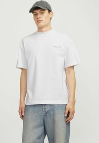 Camiseta blanca de algodón de manga corta, con un pequeño logo rojo en el pecho. Combinada con unos jeans de mezclilla azul claro. Textura suave.