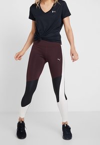 Zwarte v-hals t-shirt geknoopt in de taille, gecombineerd met bordeauxrode, zwarte en witte panel leggings. Zwarte sportschoenen maken de outfit compleet.