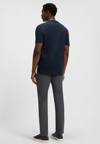 Mörkblå kortärmad skjorta med rund halsringning och rak passform, kombinerad med gråbyxor och mörka sneakers. Enkel, ren design.