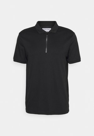 Zwart poloshirt met korte mouwen, halve ritssluiting aan de voorkant en kraag, Calvin Klein-label zichtbaar aan de binnenkant van de hals.