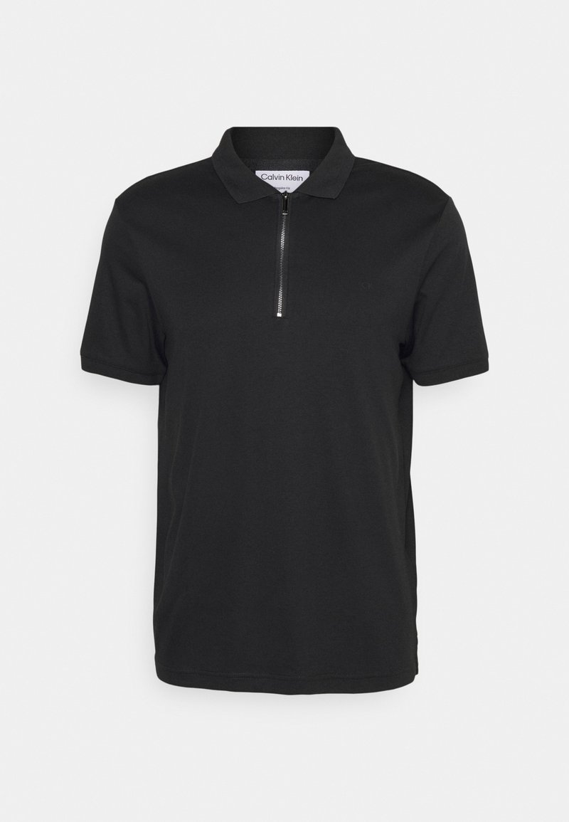 Polo noir à manches courtes avec demi-fermeture éclair à l'avant et col, étiquette Calvin Klein visible à l'intérieur de l'encolure.
