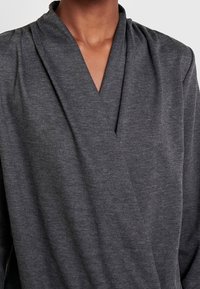 Szary top z zakładką o głębokim dekolcie w kształcie litery V, wykonany z miękkiej, teksturowanej tkaniny. Zdobiony drapowanymi detalami wokół dekoltu i ramion.