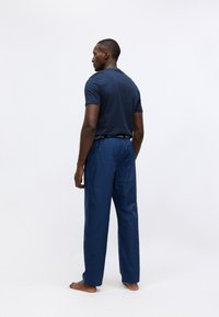 Mornarska majica i plave prugaste gaće za opuštanje s elastičnim pojasom. Gaće imaju širok kroj i glatku teksturu. Jednostavna pozadina.