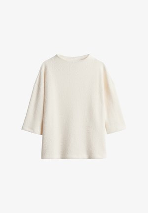 Haut long à manches larges de couleur blanc cassé, avec une coupe ample et un col rond simple.