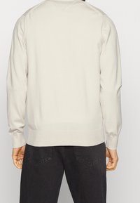 Jersey de punto gris claro con mangas largas, puños y dobladillo acanalados, hecho de un material suave y liso. Presenta un diseño simple y limpio.