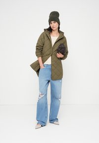 Χακί καπιτονέ μπουφάν με κουκούλα, ανοιχτό μπεζ τοπ, φαρδιά τζιν παντελόνια με φθορές, γκρι σκουφί και μικρή μαύρη τσάντα.