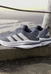 Gray athletic shoes with white three-stripe logo, textured mesh upper, cushioned Cloudfoam sole, and a rounded toe design.
