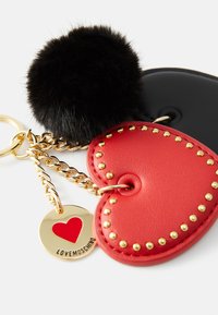 Red heart-shaped leather keychain with gold studs, attached to a black faux fur pompom and a gold round tag featuring a red heart.