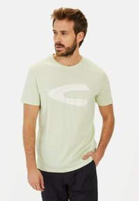 Lysegrøn bomulds T-shirt med rund halsudskæring og korte ærmer, der har et stort hvidt logo designet på forsiden.