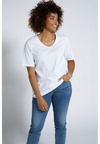 Bílý bavlněný tričko s výstřihem do V a krátkým rukávem, v kombinaci s modrými džíny. Materiál je hladký, bez viditelných vzorů nebo akcentů.