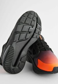 Baskets de sport noires avec un design dégradé allant de l'orange au noir, semelles texturées et lacets. Accents en maille notables et détails de rembourrage supplémentaires.