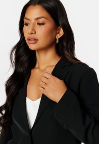 Czarna marynarka o dopasowanym kroju, z wyraźnymi klapami i czterema guzikami na mankietach, zestawiona z białą bluzką o głębokim dekolcie w kształcie V.