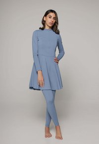 Lichtblauwe lange mouw jurk met een aansluitend lijfje en een uitlopende rok, gecombineerd met bijpassende legging. Glad materiaal met een subtiele glans.