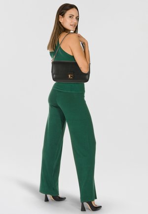 Borsa a tracolla in pelle nera con finitura testurizzata e dettagli in oro. Modello con outfit verde, che indossa pantaloni a taglio ampio e scarpe con tacco.