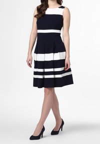 Námořnické šaty s bílými vodorovnými pruhy, bez rukávů, s přiléhavým živůtkem a skládací sukní. Nosené s námořnickými lodičkami na vysokém podpatku.