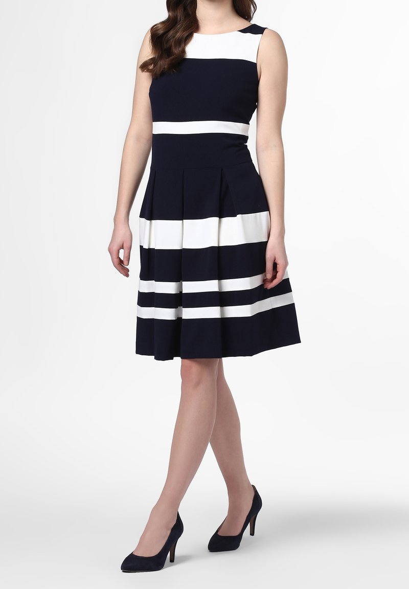 Námořnické šaty s bílými vodorovnými pruhy, bez rukávů, s přiléhavým živůtkem a skládací sukní. Nosené s námořnickými lodičkami na vysokém podpatku.