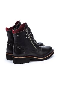 Stivaletti in pelle nera con cerniera laterale, fodera interna rossa, dettagli decorativi con borchie e suola nera spessa.