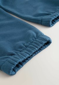 Pantalons de survêtement en coton bleu avec des poignets élastiques aux chevilles et une texture douce et lisse, disposés à plat sur une surface claire.