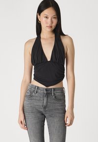 Top negro tipo halter hecho de una tela suave con un escote en V profundo, centro fruncido y un diseño de dobladillo puntiagudo; combinado con jeans grises de talle alto.