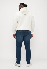 Krem dukserica s podesivom kapuljačom, uparena s tamnoplavim uskim trapericama. Outfit upotpunjuju svijetlosive atletske tenisice.