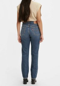 Jeans de denim azul de talle alto con corte recto, que cuentan con un parche de cuero en la parte posterior, dos bolsillos traseros y detalles de costura sutiles.