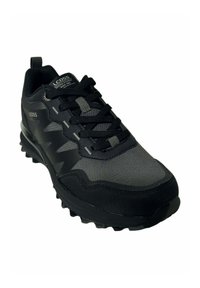 Zapatilla deportiva negra con parte superior de malla, puntera reforzada, suela de goma gruesa con surcos de tracción y acentos texturizados en contraste.