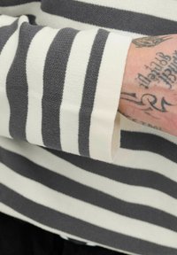 Striped long-sleeve shirt in beige and dark gray, featuring a ribbed texture and visible cuff with a rolled detail.
