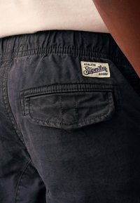 Mørkeblå shorts med elastisk taljebånd, med en laplomme og et vævet mærke med teksten "Superdry" i creme og navy.