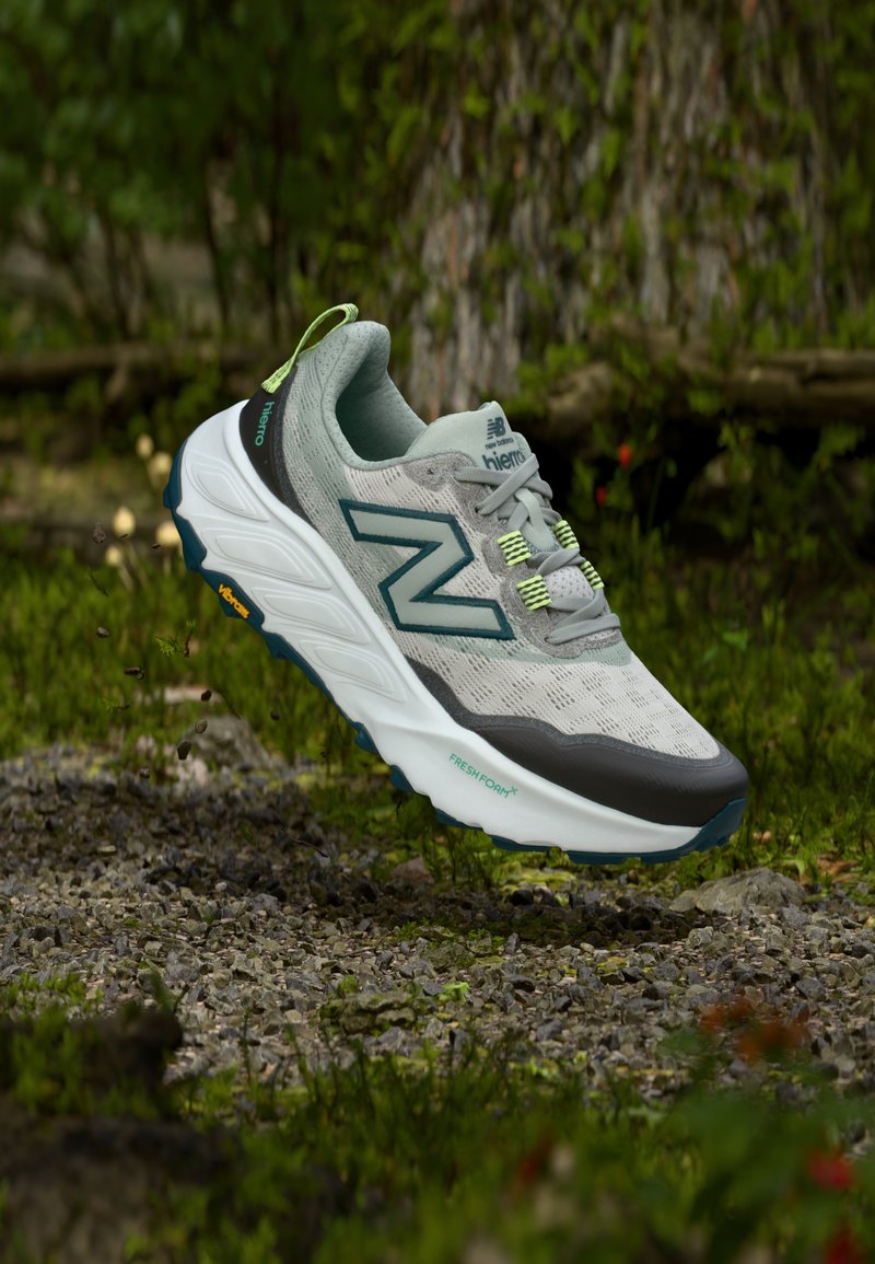 Chaussure de sport gris clair avec une tige en mesh texturé, des accents verts et une semelle intermédiaire blanche épaisse, dotée d'une semelle extérieure en caoutchouc Vibram.