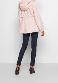 Ljusrosa hoodie-jacka med elastisk midja, långa ärmar och en slät textur. Kombinationen med mörkblå tajta jeans och bruna klackskor.