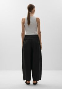 Pantalons larges noirs à taille haute, fabriqués dans un tissu doux. Associés à un débardeur blanc ajusté. Vue de l'arrière.