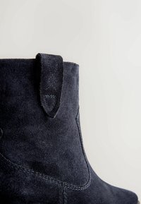 Stivale alla caviglia in suede blu navy con superficie texturizzata, pannello elastico laterale e linguetta sul tallone, arricchito da dettagli di cucitura a contrasto.