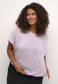 Helles rosa, locker geschnittene Bluse mit kurzen Ärmeln und rundem Ausschnitt, aus einem weichen, strukturierten Stoff, kombiniert mit dunkelfarbigen Hosen.