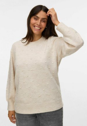 Light beige knitted sweater with textured bobble details, round neck, and long sleeves, paired with gray pants. Soft and relaxed fit.