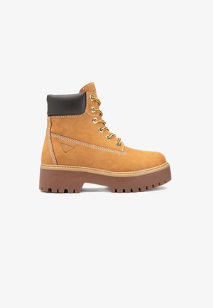 Stivaletto alla caviglia in pelle marrone chiaro con lacci, collo imbottito marrone scuro e suola spessa marrone con tacche, vista laterale su sfondo bianco.