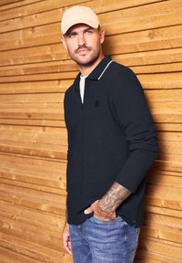 Námořnická dlouhá polo košile se zipem na límci, s kontrastním bílým detailem na výstřihu, v kombinaci se světle modrými džíny.